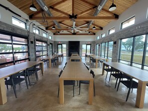 A spacious indoor area with long tables and chairs, large windows, and a high wooden ceiling with exposed beams. - Charming Tiny Home for five guests in Fredericksburg TX (Fredericksburg)