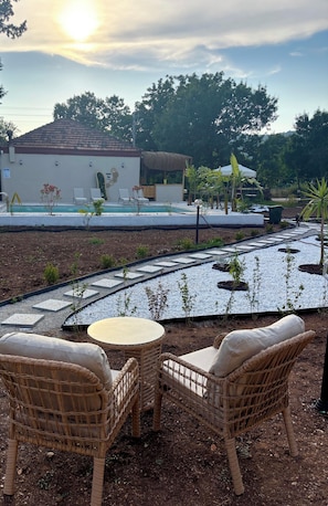 Un jardín con mobiliario de mimbre, piscina y un edificio con tejado de azulejos.