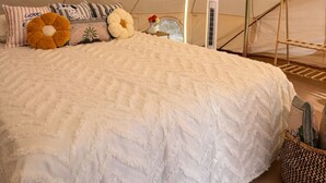 Una tenda con un letto, cuscini, un tavolino con un vaso e un appendiabiti.