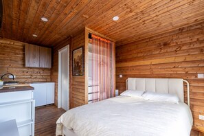 A wooden-paneled room with a bed, a white desk, and a door.