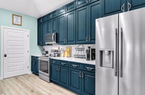 A kitchen with teal cabinets, stainless steel appliances, and a water dispenser. - Shrimper and Grits, New Construction, Private Pool, Short Walk to Beach, Beach Gear Credit (St. George Island)