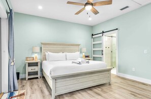 A bedroom with a bed, nightstands, a ceiling fan, and a sliding glass door. - Shrimper and Grits, New Construction, Private Pool, Short Walk to Beach, Beach Gear Credit (St. George Island)