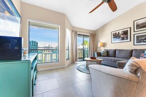 A modern living room with a television, sofa, and a balcony with a view. - Ocean Mile K-10, Poolside views, Beach View, Beach Gear Credit with Booking (St. George Island)