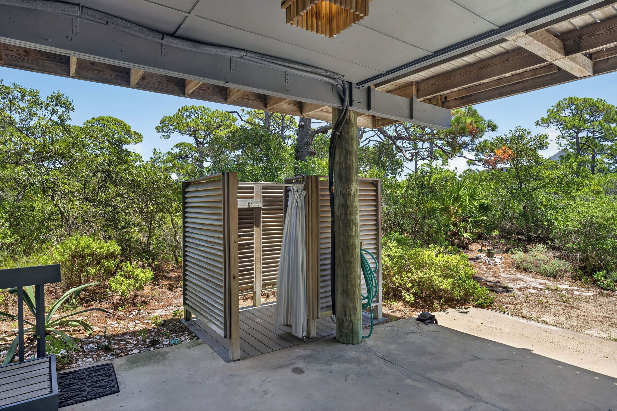 A covered outdoor area with a wooden structure, a concrete floor, and a view of surrounding vegetation.