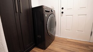Un appareil compact combinant lave-linge et sèche-linge, placé dans une pièce dont le sol est recouvert de parquet et qui possède une porte blanche.