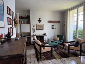 Ein Wohnzimmer mit einer Couch, Sesseln, einem Couchtisch, einem Bücherregal und einem großen Fenster.
