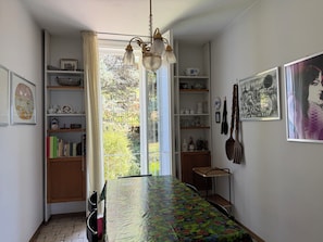 Ein Zimmer mit Esstisch, Regalen voller Gegenstände, einer Hängelampe und einem Fenster mit Vorhängen.