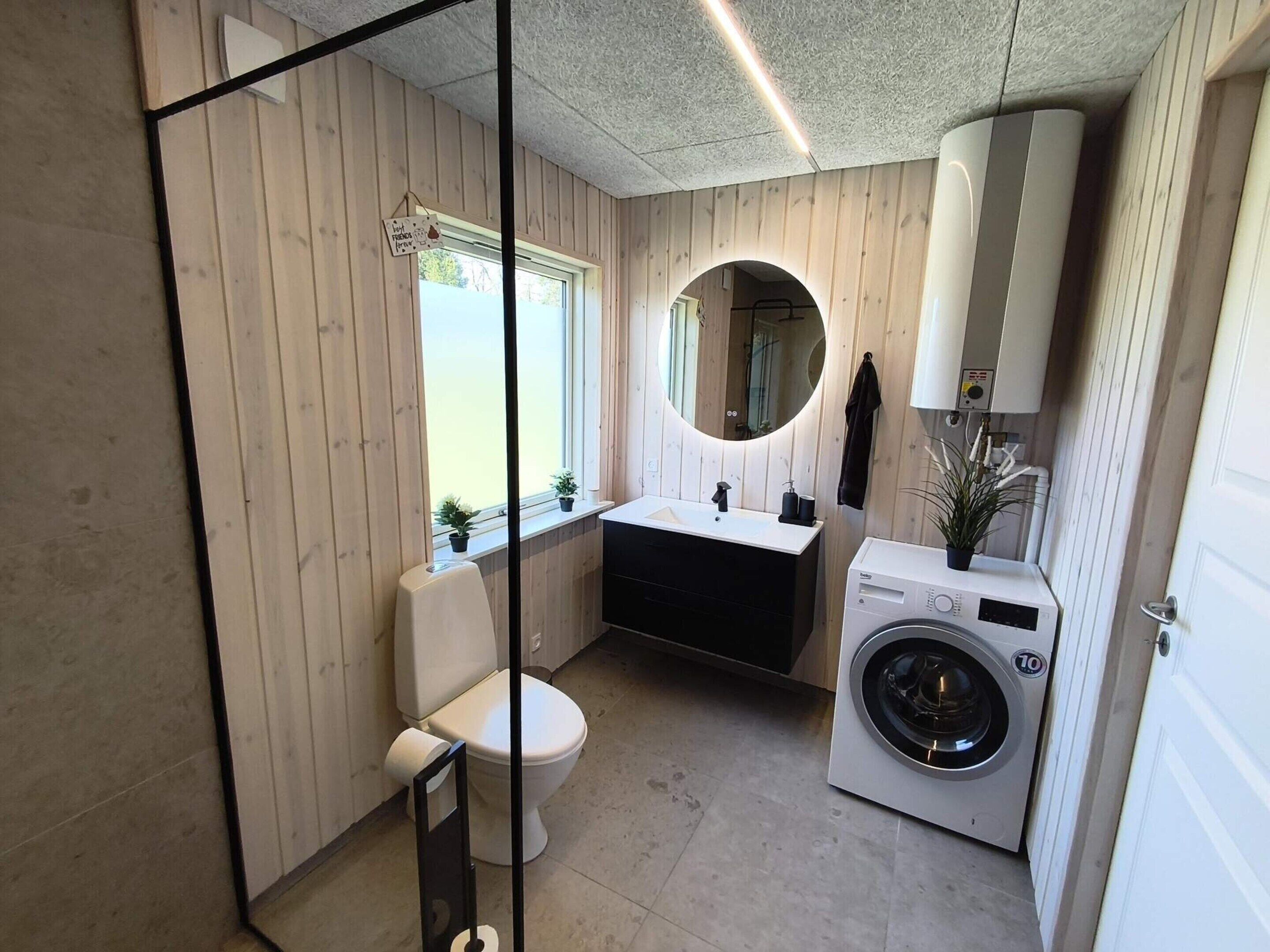 Une petite salle de bain comprenant des toilettes, un lavabo, un miroir et un lave-linge.
