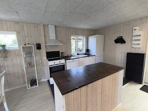 A compact kitchen with wooden panel walls, a central island, a built-in oven, and a window. - 4 Star Holiday Home in Vaeggerlose (Vaeggerlose)