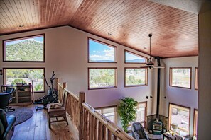 A spacious room with multiple large windows, a wooden ceiling, and a view of a mountainous landscape.