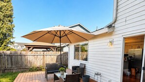 A wooden deck with outdoor furniture, a large umbrella, and a sliding glass door leading to a kitchen. - 4 BD, Pet Friendly - Modern chic beautiful, fenced yard (Vancouver)
