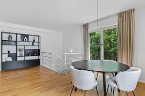 Una habitación moderna con una mesa redonda, dos sillas, una estantería blanco y negro y un gran ventanal con cortinas.
