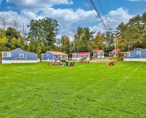 A row of blue cabins with red roofs, a grassy lawn, and a picnic area with chairs.