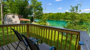 Eine Holzterrasse mit Stühlen mit Blick auf einen See, umgeben von Bäumen und einem Haus.