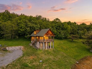 Eine Holzhütte mit Balkon, umgeben von üppiger Vegetation und Bäumen.