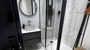 A modern bathroom with a glass-enclosed shower, a round mirror, and a marble wall. - 8-enclosure room - BS HOUSE HÔTEL (Pointe-à-Pitre)