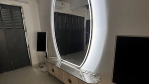 A vanity with a large mirror, a vanity table, a flat-screen TV, and a wall-mounted speaker. - 8-enclosure room - BS HOUSE HÔTEL (Pointe-à-Pitre)