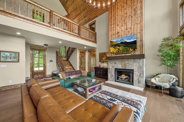 A spacious living area with a fireplace, leather sofa, and a staircase leading to an upper level. - Luxury Mountain Retreat in Eagles Nest (Banner Elk)