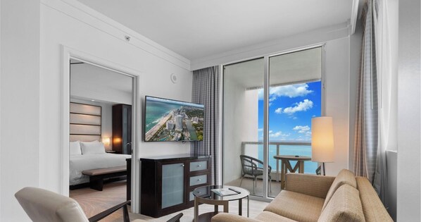 A hotel room with a bed, a TV, a desk, a chair, a sofa, and a balcony with a view of the ocean. - Sorrento 1514 (Miami Beach)
