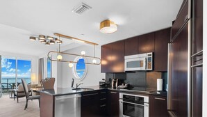 A modern kitchen with stainless steel appliances, dark wood cabinets, and a large window overlooking a scenic view. - Sorrento 1514 (Miami Beach)