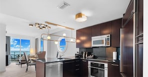 A modern kitchen with stainless steel appliances, dark wood cabinets, and a large window overlooking a scenic view. - Sorrento 1514 (Miami Beach)