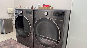 Un área de lavandería con dos lavadoras LG ThinQ de carga frontal, un pequeño bote de basura y un objeto decorativo rojo encima.