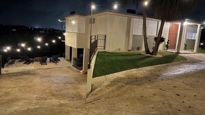 Un edificio moderno con una zona de estar al aire libre techada, un pequeño césped y una escalera que conduce a un nivel superior.