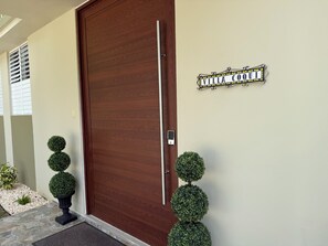 Una puerta marrón con manija de metal, un letrero que dice 'VILLA COQUI' y dos plantas de boj esféricas a cada lado.