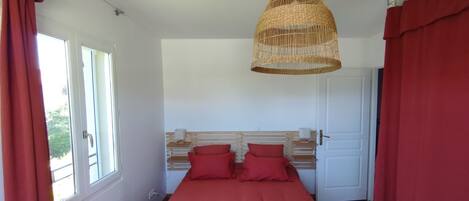 A bedroom with a bed, a hanging wicker lamp, a window, and a door.