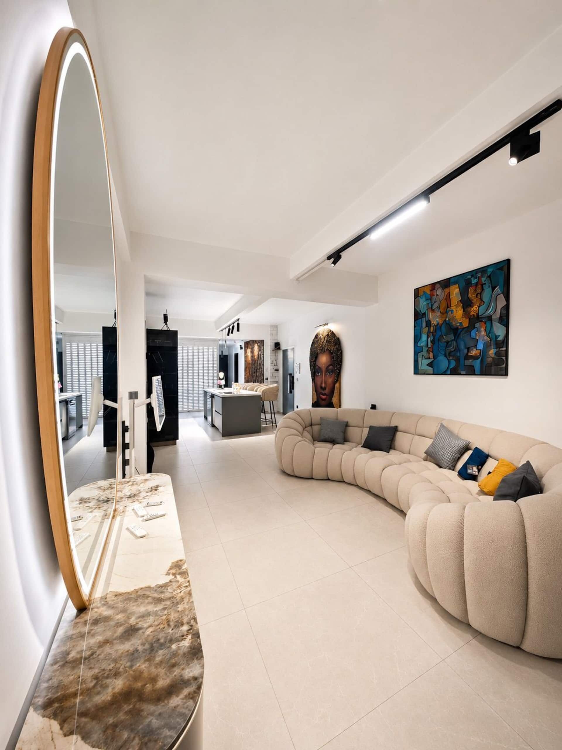 A modern living room with a curved sofa, a large mirror, and a painting on the wall.