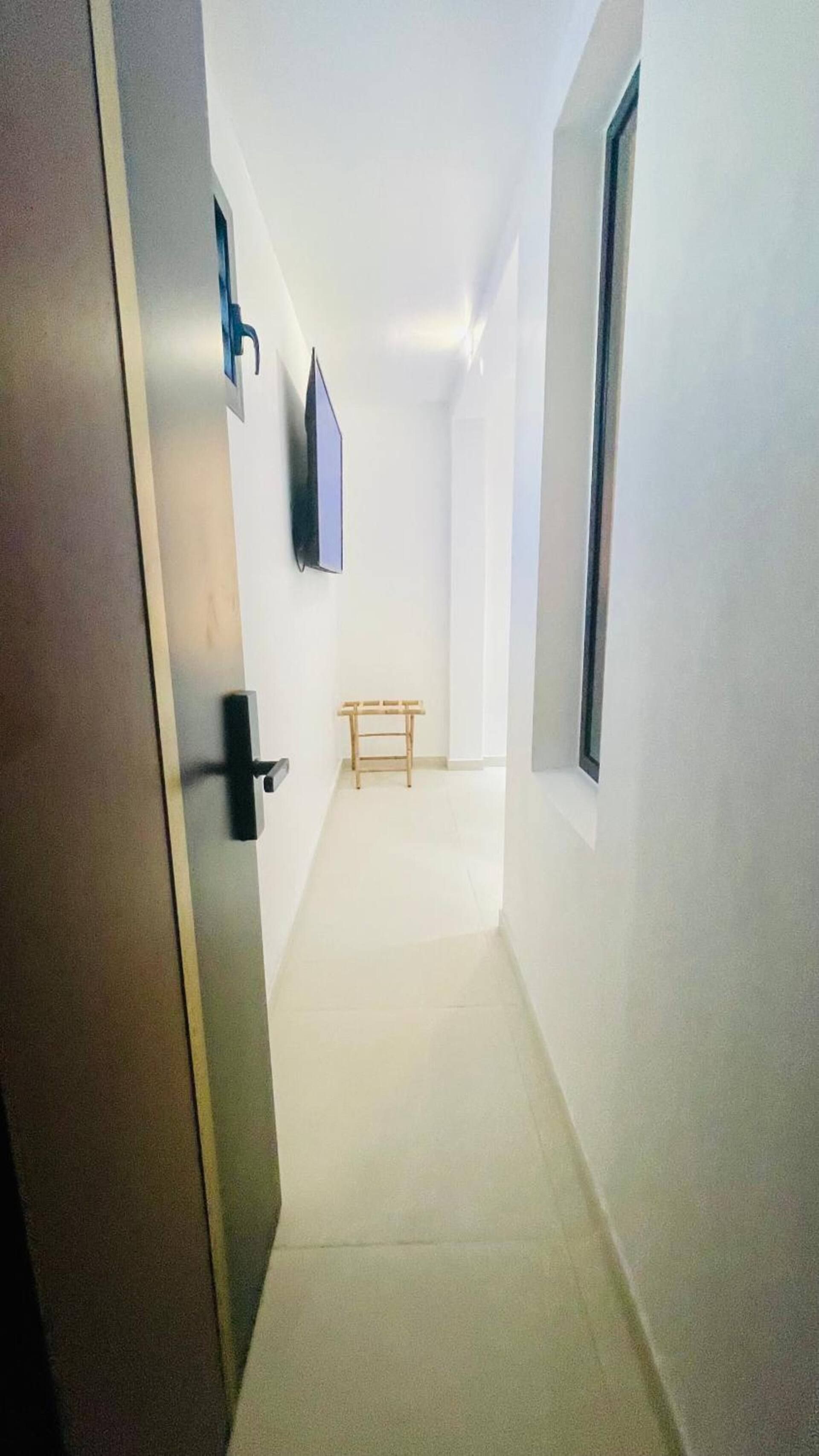 Un corridoio stretto con una panca di legno, una porta a sinistra e una finestra a destra.