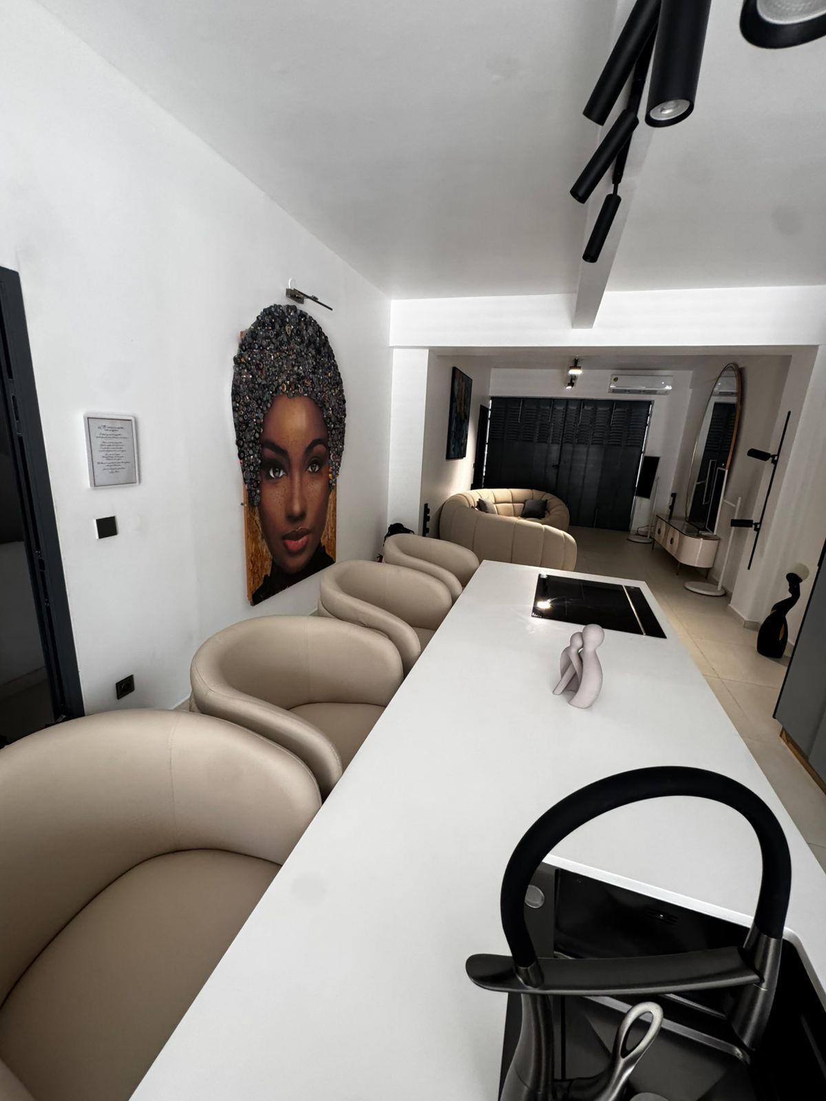 A modern interior with a long dining table, beige upholstered chairs, and a large wall-mounted artwork.
