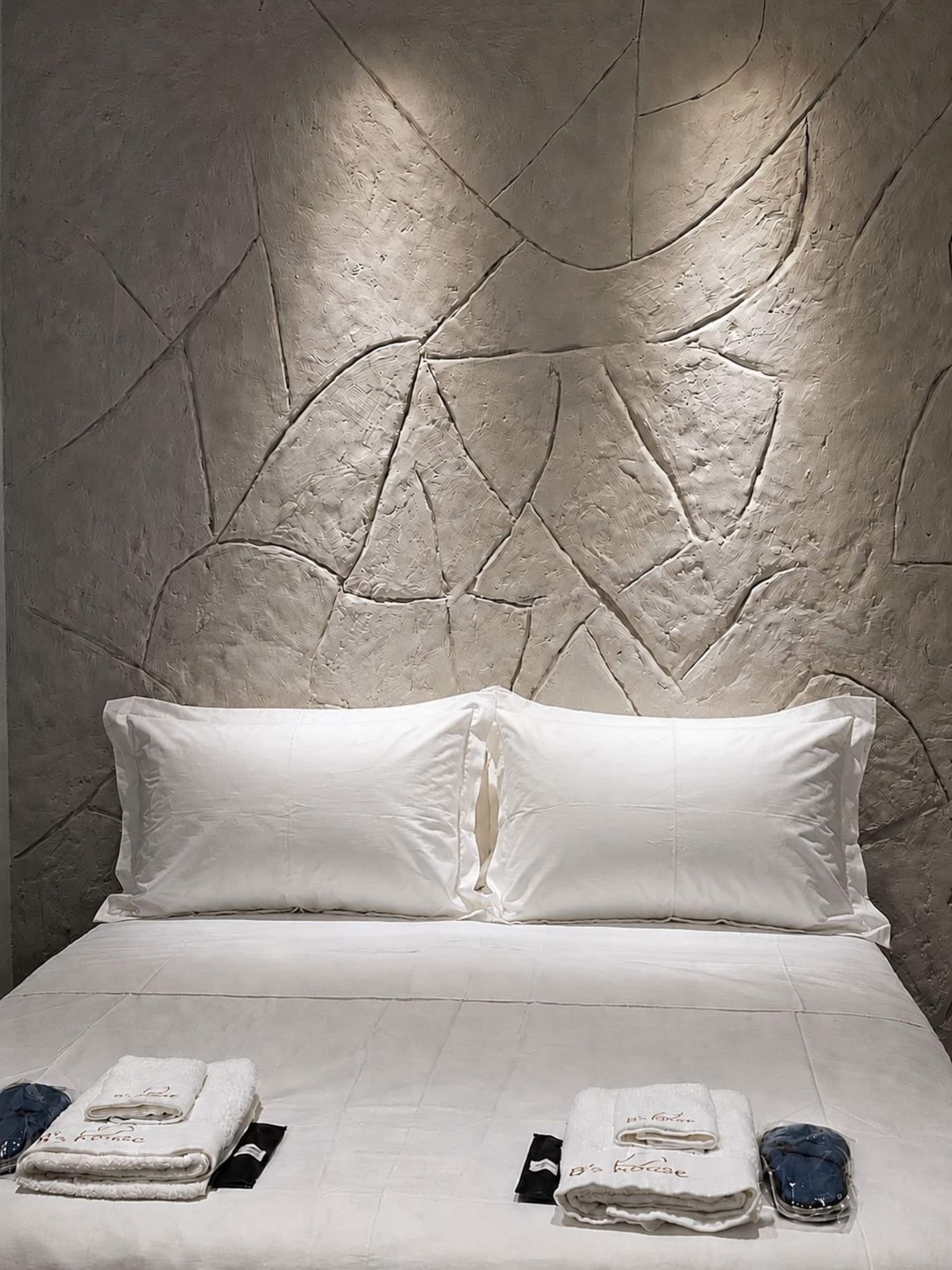A bed with white linens, two pillows, and a folded towel with text on it.