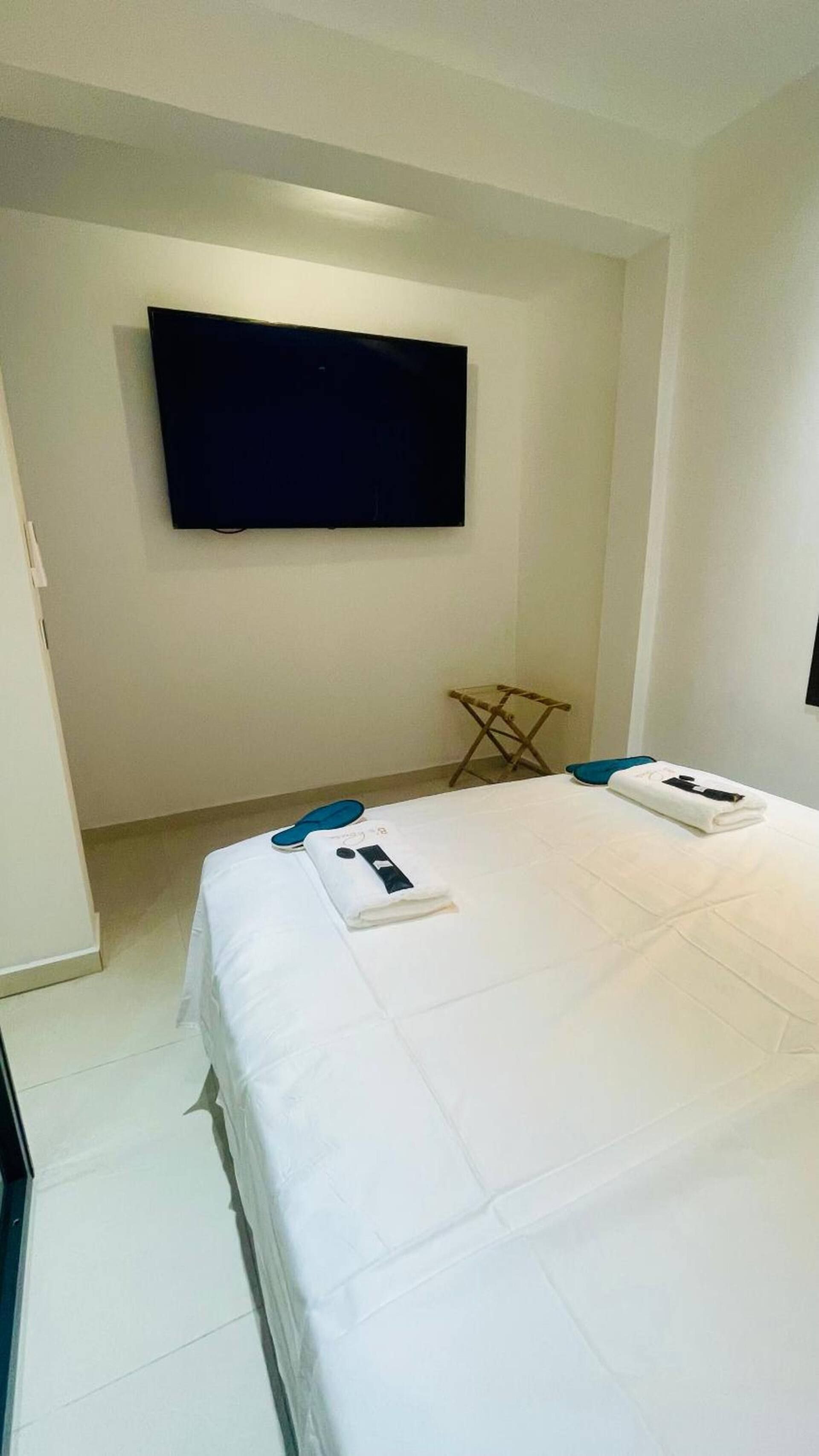 A hotel room with a bed, a flat-screen TV mounted on the wall, and a small folding table.