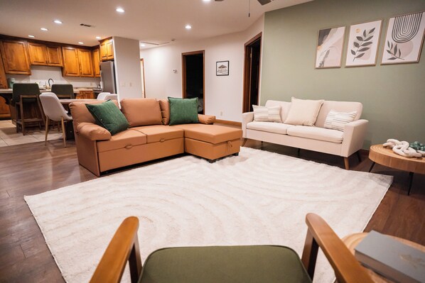 A living room with a sectional sofa, a separate sofa, a round coffee table, and a dining area with chairs and a table.