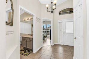 A hallway with a mirror, a chandelier, a sign saying 'TOGETHER we make a family,' and a view into a bedroom. - Disney World Retreat Oasis, Pool, Privacy & Comfort. (Kissimmee)