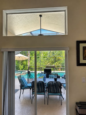 A room with a sliding glass door leading to an outdoor area with a pool and lounge chairs. - Disney World Retreat Oasis, Pool, Privacy & Comfort. (Kissimmee)