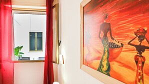 Ett hotellrum med ett stort fönster, en tavla på väggen och en röd gardin.
