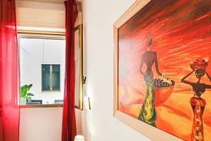 Ein Hotelzimmer mit großem Fenster, einem Gemälde an der Wand und einem roten Vorhang.