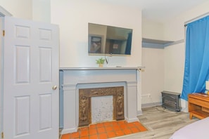 A room with a white door, a fireplace with a blue mantel, a television mounted above it, and a blue curtain on the right.