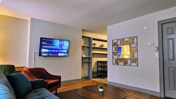 Una sala de estar con sofá, sillón, mesa de centro, televisor, estanterías y una puerta.
