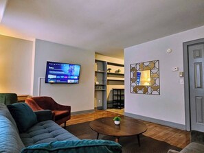 Una sala de estar con sofá, sillón, mesa de centro, televisor, estanterías y una puerta.