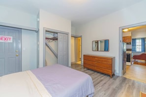 A bedroom with a bed, a dresser, a mirror, and a door marked 'Emergency Exit Only'.