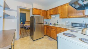 Una cocina compacta con armarios de madera, un refrigerador de acero inoxidable, un microondas, una estufa y un lavamanos.