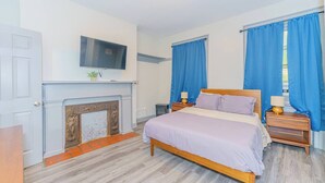 Un dormitorio con cama, televisor sobre la chimenea y cortinas azules.