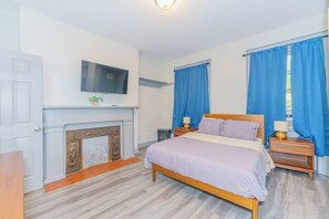 Une chambre à coucher avec un lit, un téléviseur au-dessus de la cheminée et des rideaux bleus.