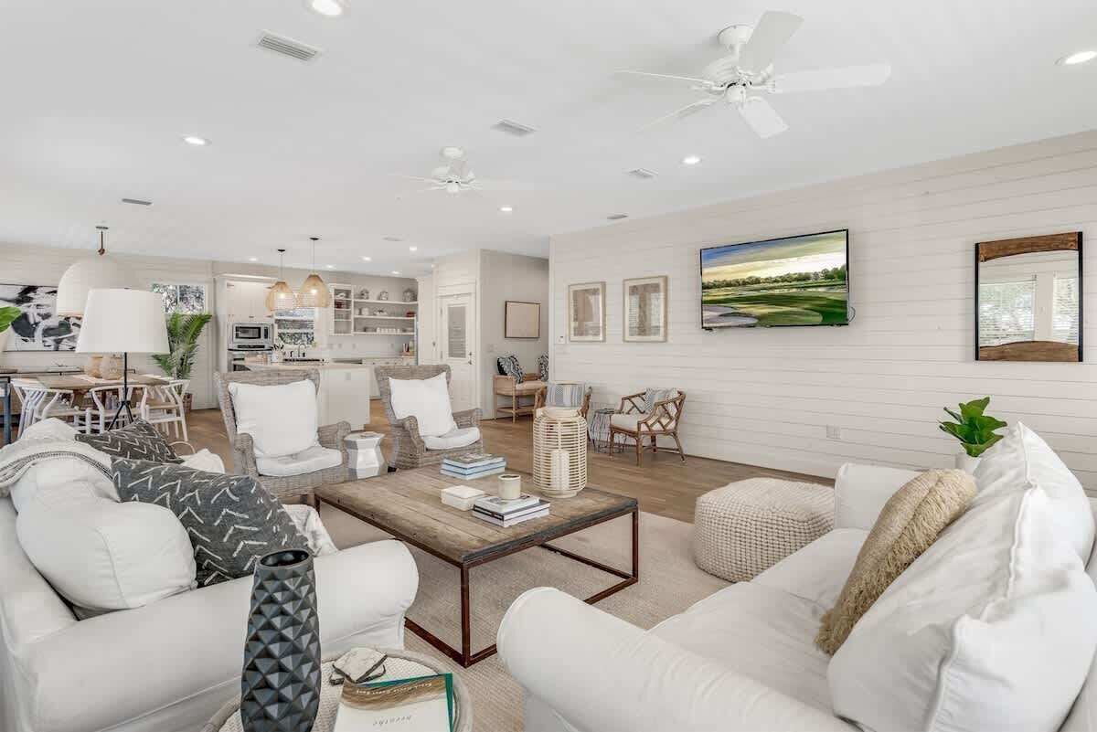A spacious living room with white furniture, a coffee table, and a TV mounted on the wall.
