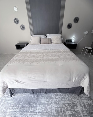 Un lit bien fait, recouvert d’une couvre-lit à motifs, une table de chevet avec une horloge et des appliques murales décoratives.