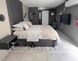 A bedroom with a bed, a chair, a TV, and a small table.