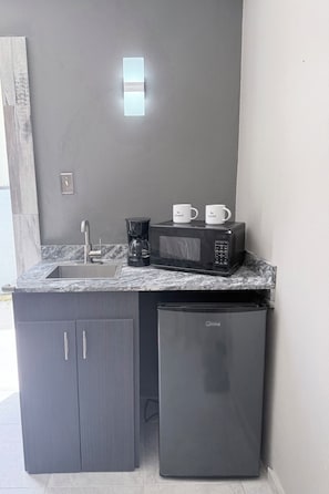 A compact kitchen with a sink, a coffee maker, a microwave, and a refrigerator.